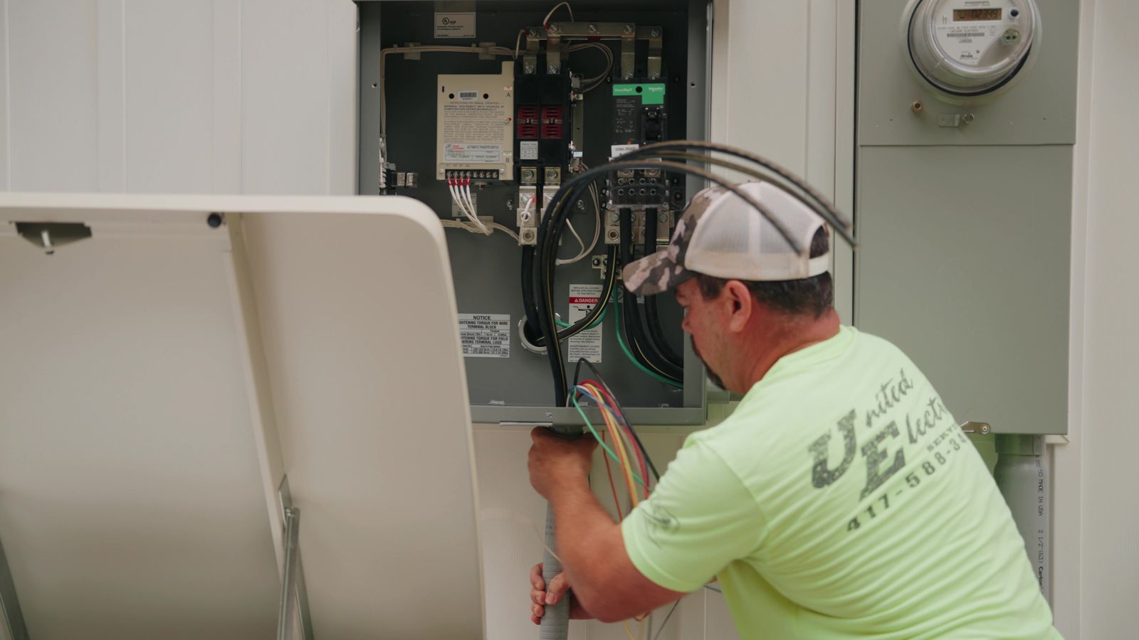 Electrician working inside an outdoor service disconnect beside the meter